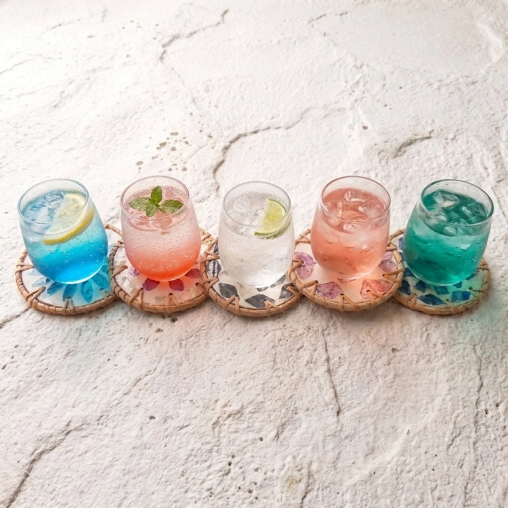 Five colorful cocktails on woven round coasters with floral mosaic detailing, arranged on a textured white surface by Bamboo Switch