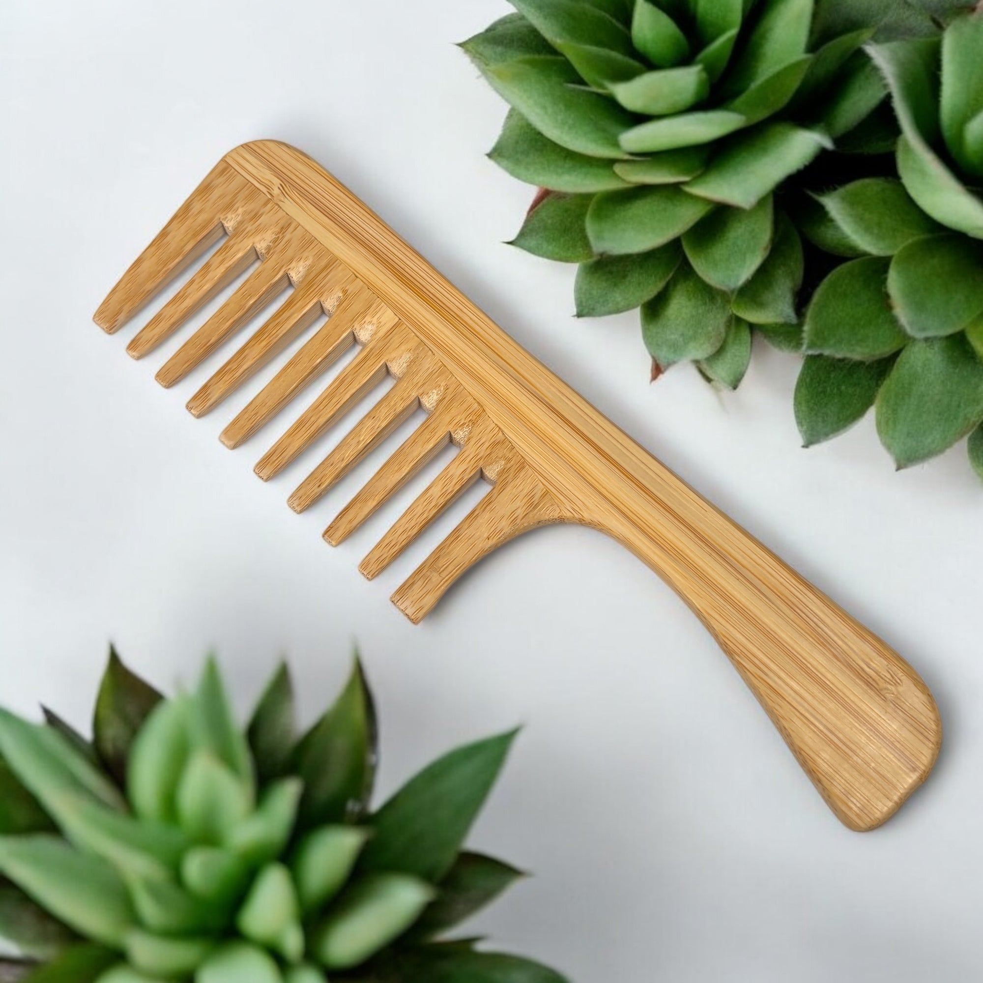 Bamboo wide tooth comb with handle and flat tips placed on white background with green succulents