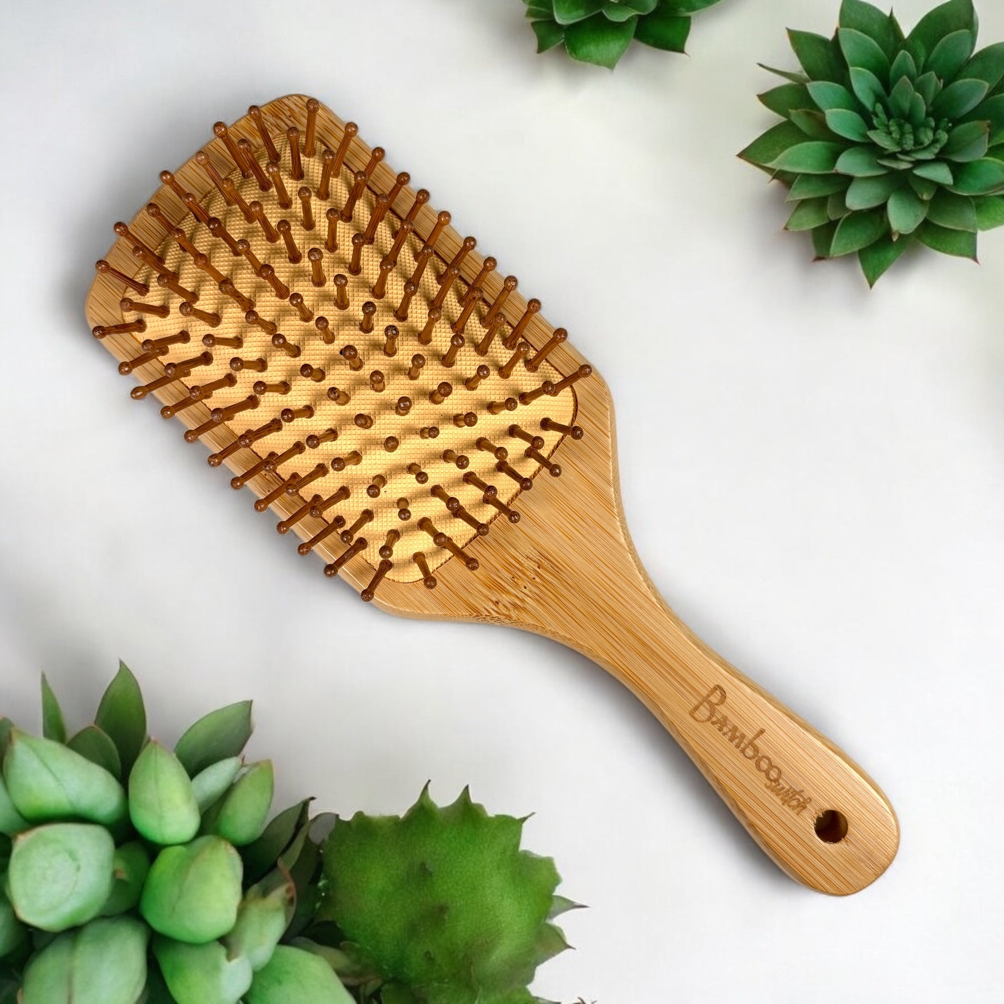 Classic bamboo paddle hair brush with wide wooden bristles on white background with succulents.