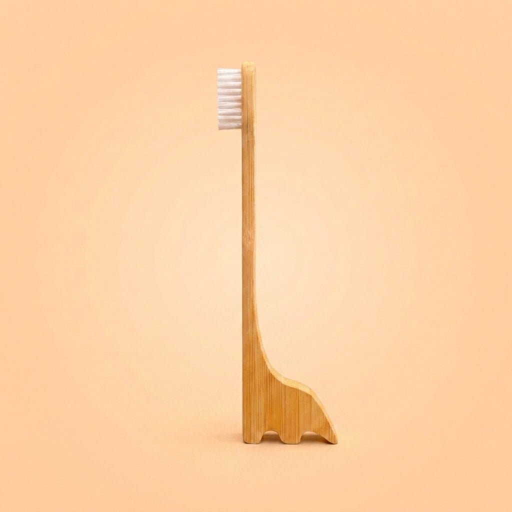 A bamboo toothbrush with a uniquely dinosaur shaped handle that doubles as a small stand, shown against a solid peach background by Bamboo Switch