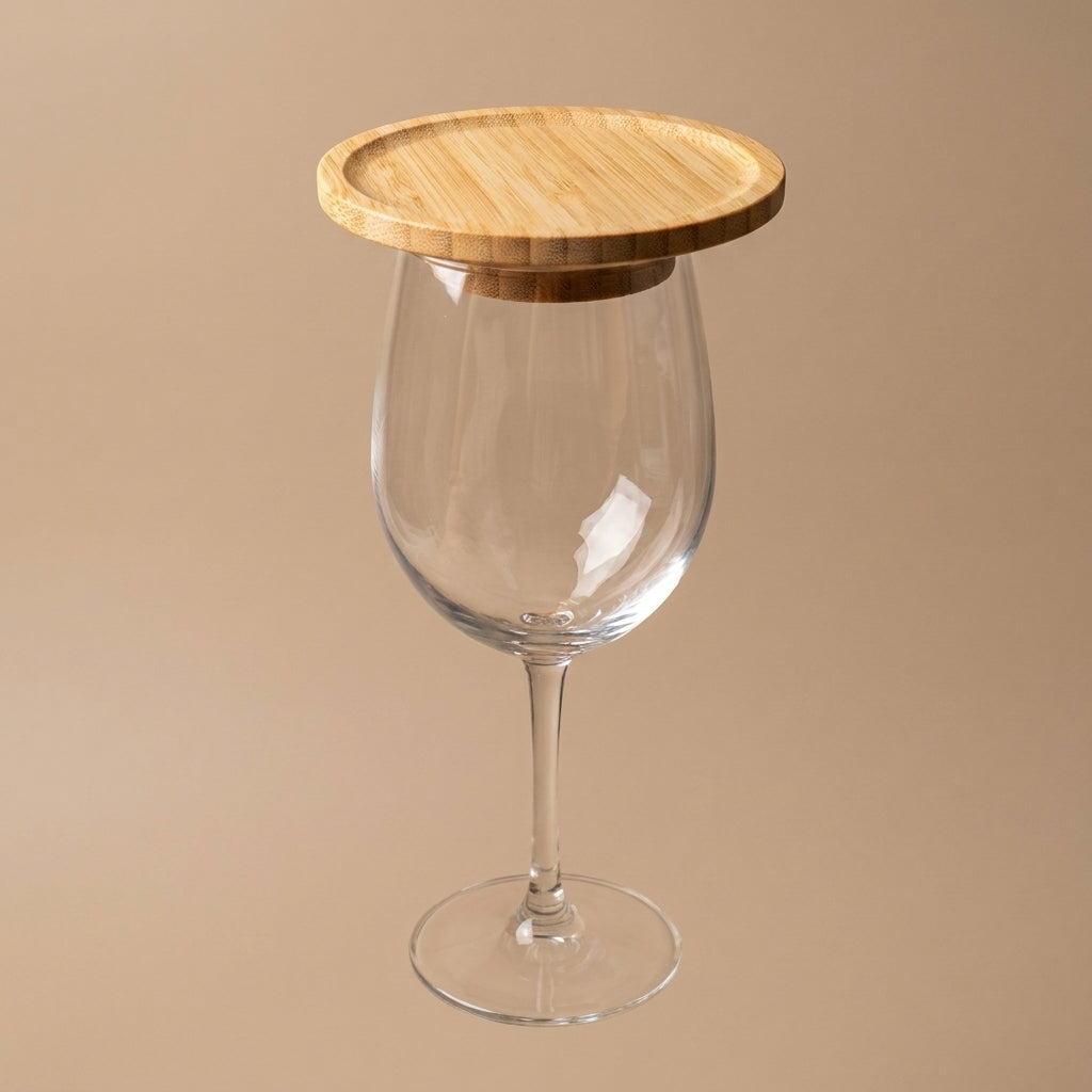 A clear wine glass with a round light wood lid resting on its rim, set against a solid beige background by Bamboo Switch