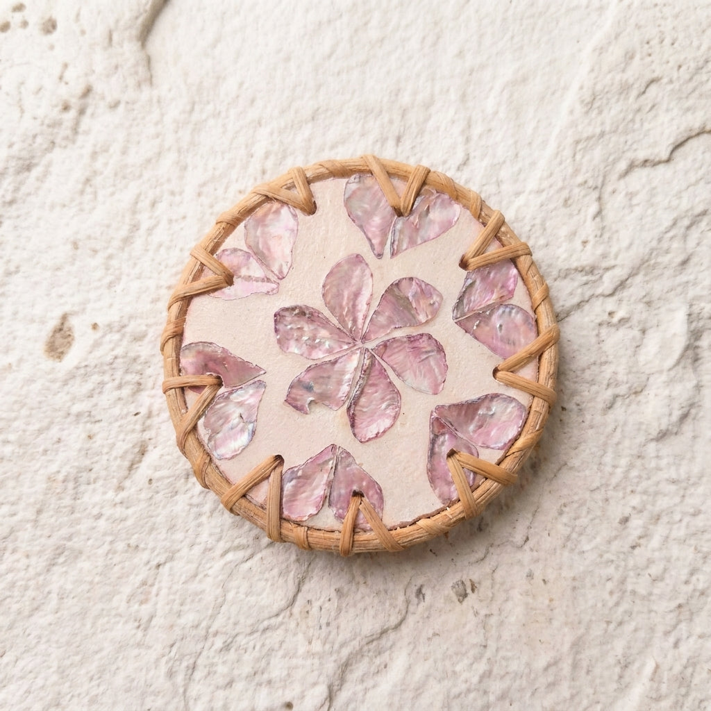 A woven and shell coaster featuring a central pink mother-of-pearl flower motif, surrounded by a tan woven border on a textured off-white background  by Bamboo Switch