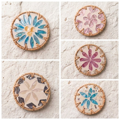 Five round woven coasters with floral and geometric tile designs in blue, pink, and beige, arranged in a two-column grid on a textured off-white stone surface  by Bamboo Switch
