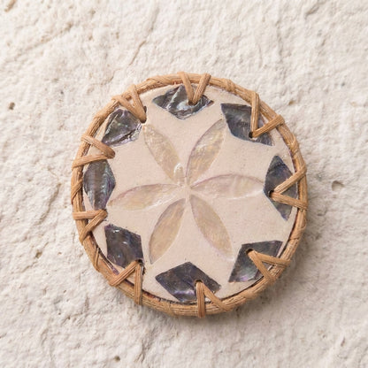 A round woven basket or tray with a natural tan wicker base, featuring a central beige floral pattern and alternating dark gray and black shell inlays around the edge, set against a textured off-white background  by Bamboo Switch