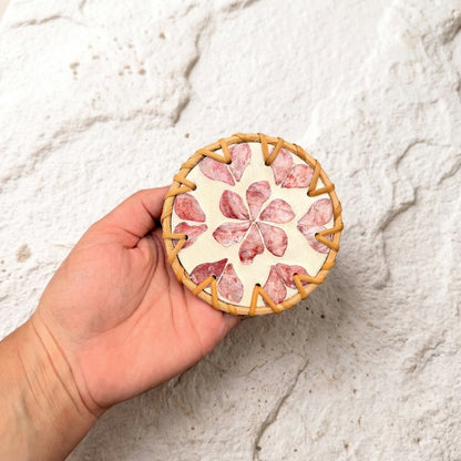 A hand holding a round ceramic coaster with a floral pattern made from sliced salami, set against a textured white stucco wall  by Bamboo Switch