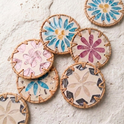 A group of round woven straw coasters with colorful floral and geometric designs, arranged on a textured off-white surface by Bamboo Switch
