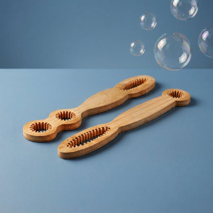 Two bamboo bubble brushes with ridged tooth-like ends and looped handles, displayed on a blue surface with floating clear bubbles in the background by Bamboo Switch