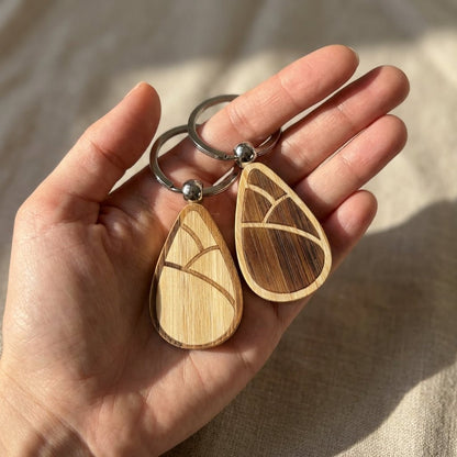 Hand holding two bamboo keychains with a natural sprout pattern.