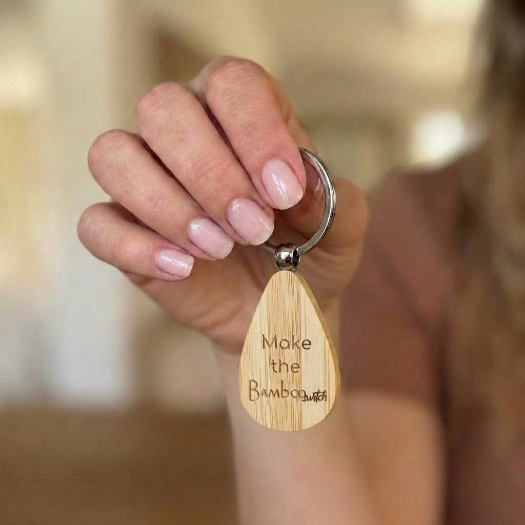 Hand holding a bamboo keychain with engraved text Make The Bamboo Switch™ against a blurred background