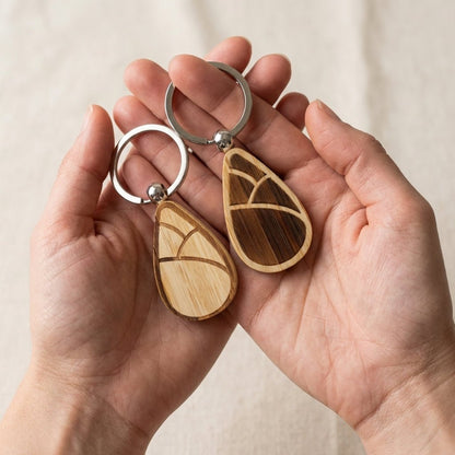 Bamboo keychains with a sprout design held in hands against a neutral background