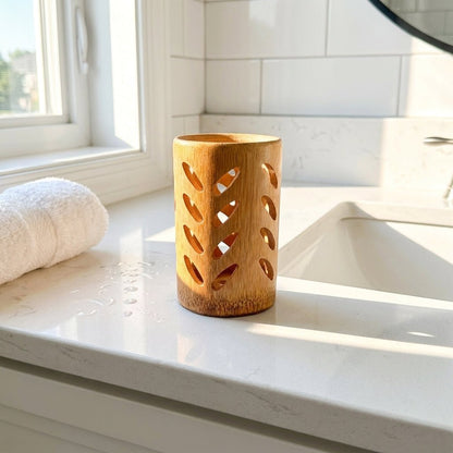 A bamboo toothbrush holder with decorative cutout patterns sits on a white marble bathroom counter next to a sink, with a white towel and window in the background by Bamboo Switch
