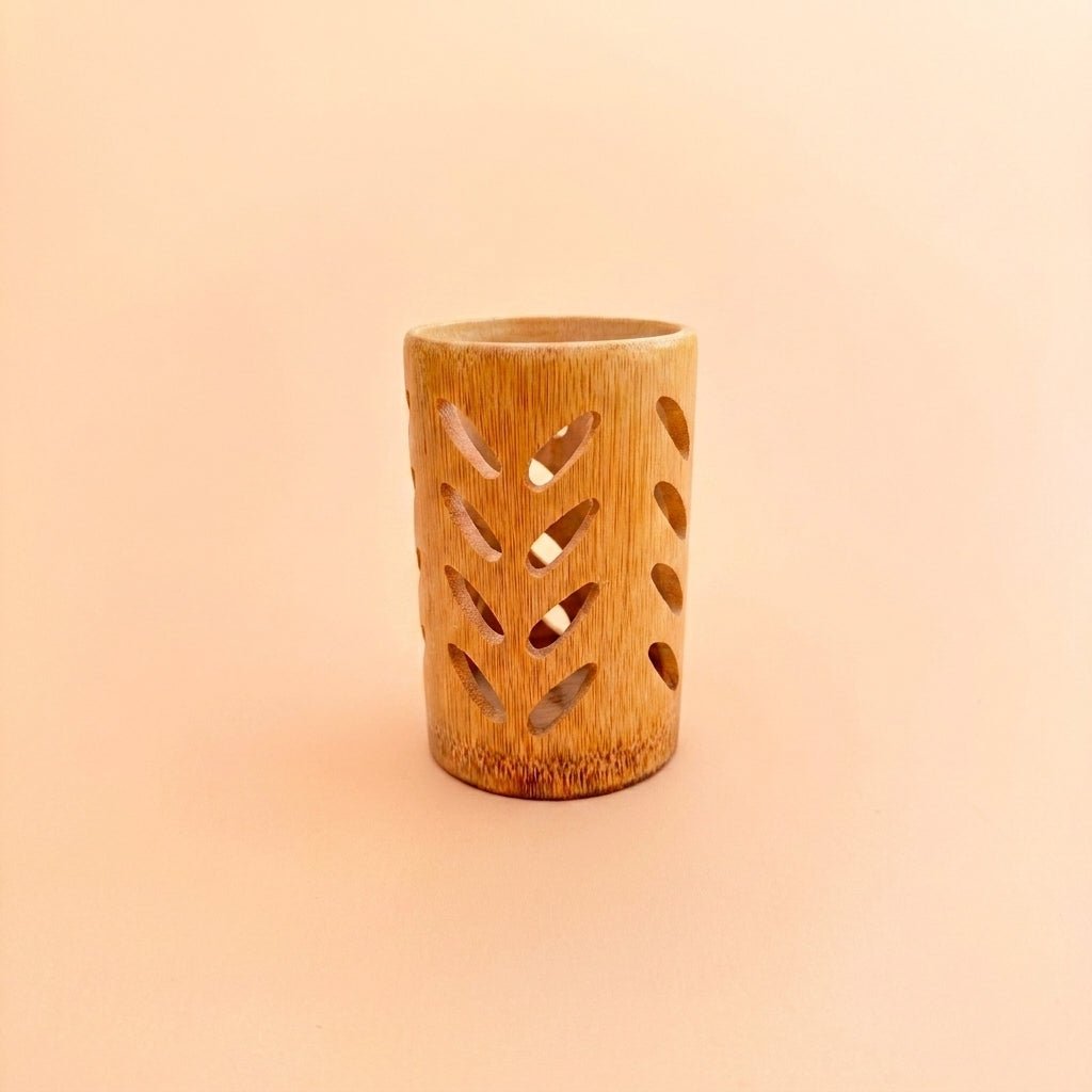 A small cylindrical bamboo holder with decorative cutout patterns, standing on a plain peach-colored background by Bamboo Switch
