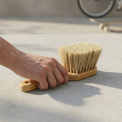 Hand holding a bamboo brush with bristles on a concrete surface.