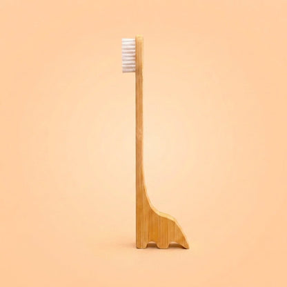 A bamboo toothbrush with a uniquely dinosaur shaped handle that doubles as a small stand, shown against a solid peach background by Bamboo Switch