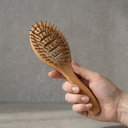 Hand holding a wooden hairbrush against a gray background