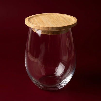 A clear glass jar with a rounded, bulbous shape and a light natural bamboo lid, set against a solid dark red background by Bamboo Switch