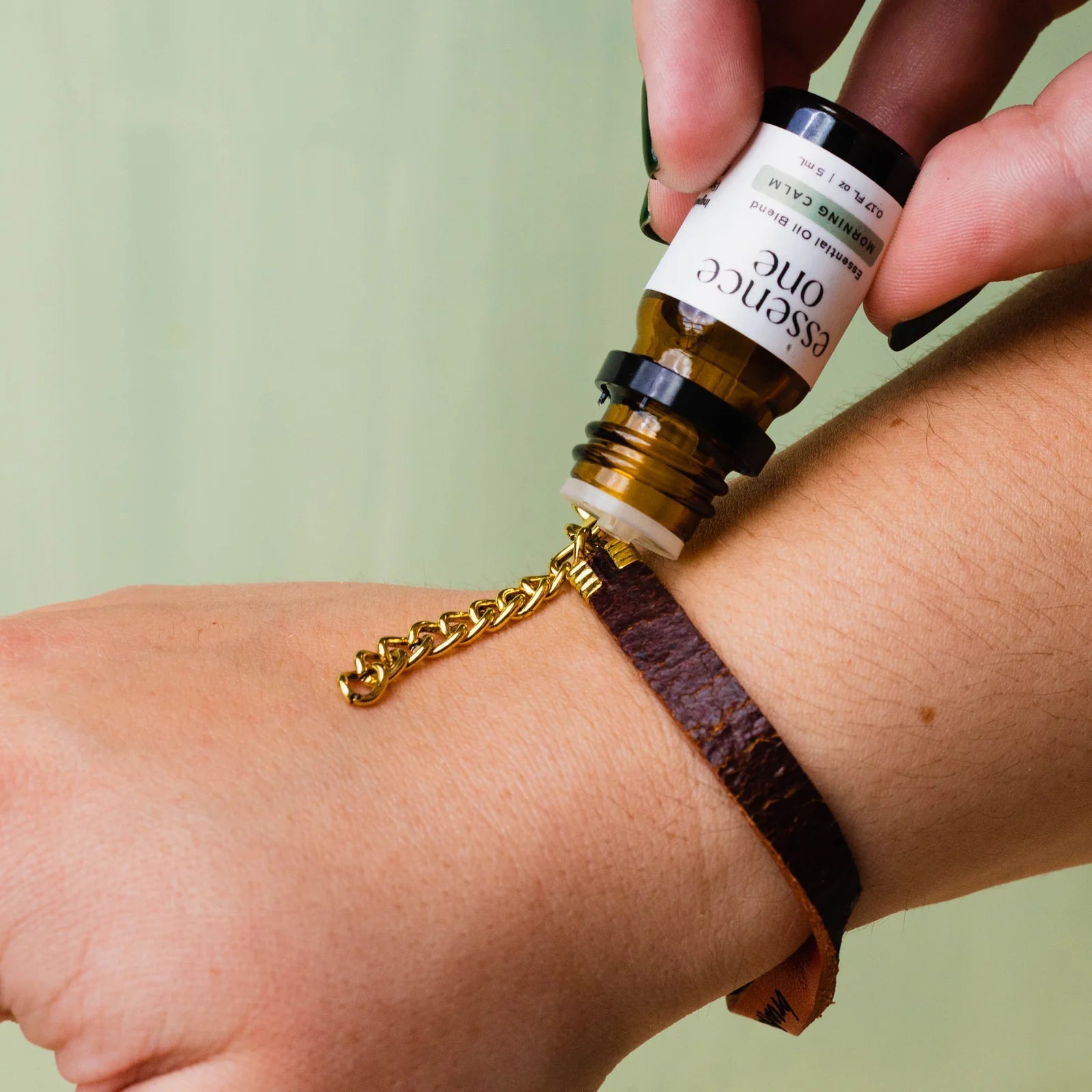 Person applying essential oil to wrist with a roller bottle labeled 'Essence One'.