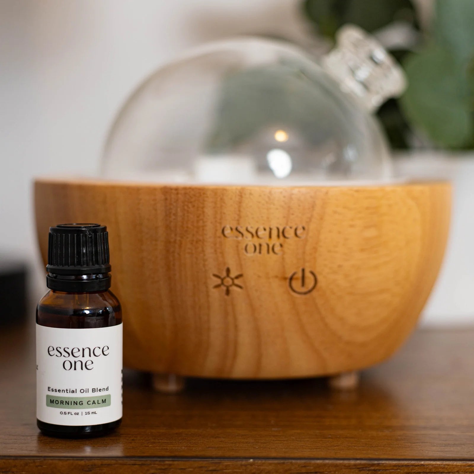 Essential oil bottle labeled 'essence one' in front of a wooden diffuser with the same branding.