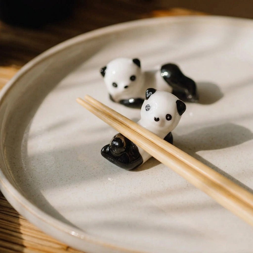 Two small panda-shaped chopstick rests on a round beige ceramic plate, with bamboo chopsticks resting across the front panda by Bamboo Switch
