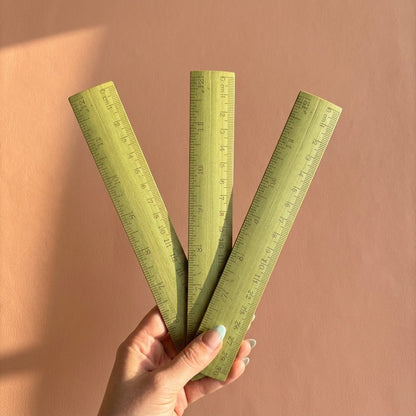 Three green bamboo rulers held by a hand against a brown background