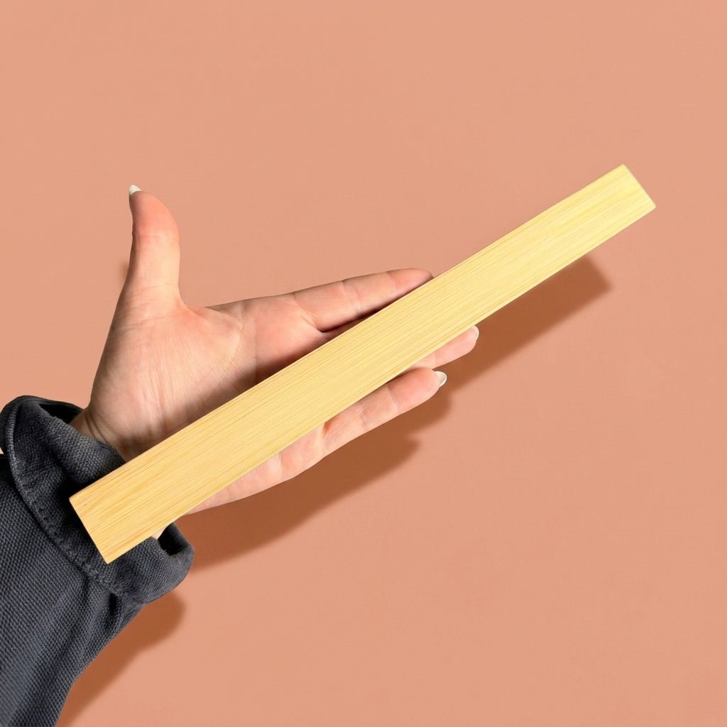 Hand holding a bamboo ruler against a beige background